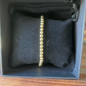May include: A gold beaded bracelet in a black velvet box.