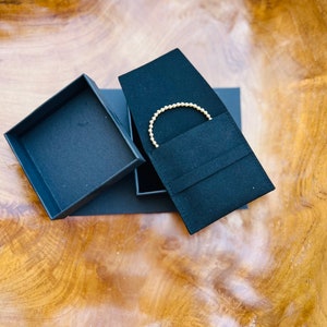 May include: A gold beaded bracelet in a black velvet jewelry box with a black cardboard box lid.