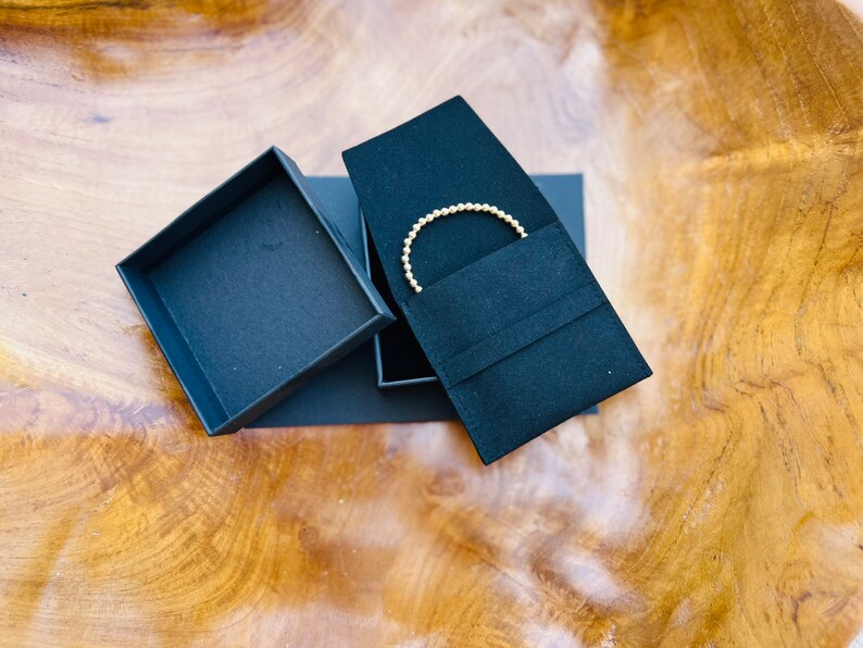 May include: A gold beaded bracelet in a black velvet jewelry box with a black cardboard box lid.