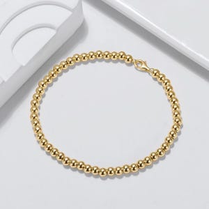 May include: A gold beaded bracelet with a simple clasp closure. The bracelet is made of small, round beads that are evenly spaced.