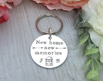 May include: Silver keychain with a round tag that says "New home new memories" with a house icon and the letters "J" and "B" on either side of the house.