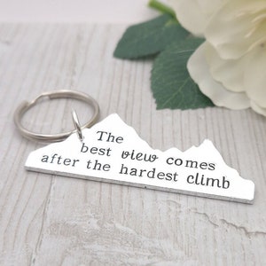 May include: Silver mountain-shaped keyring with the text "The best view comes after the hardest climb".