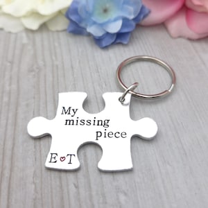 May include: A silver puzzle piece keyring with the words "My missing piece" and the initials "E ♡ T" engraved. The keyring has a silver ring attached. Flowers are in the background.