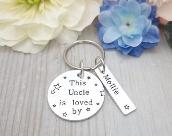 May include: Silver keychain with a round charm that says "This Uncle is loved by" with stars around the text. A smaller silver tag with the name "Mollie" is attached to the keychain.