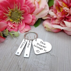 May include: Silver keyring with three tags. The tags are engraved with the names "Chloe", "Eva", and "This Mummy belongs to". The keyring has a heart-shaped charm with two small hearts engraved on it.