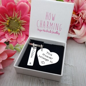 May include: A silver heart-shaped keyring with the text "This Mummy belongs to" and a smaller heart with two hearts inside. A silver rectangular tag with the name "Chloe" and a small heart is attached to the keyring.