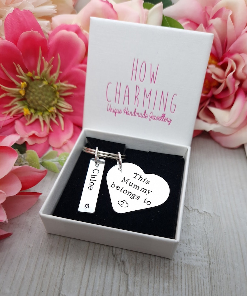 May include: A silver heart-shaped keyring with the text "This Mummy belongs to" and a smaller heart with two hearts inside. A silver rectangular tag with the name "Chloe" and a small heart is attached to the keyring.