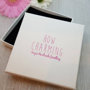 May include: White gift box with a pink lid. The lid has the text "HOW CHARMING Unique Handmade Jewellery" printed on it.
