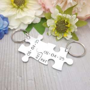 Peut inclure: Deux porte-clés en forme de puzzle en argent avec la date "08.04.25" et les initiales "H&T" gravées dessus.