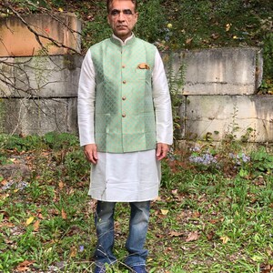 Peut inclure: Un homme portant un gilet vert clair &agrave; motif dor&eacute; et boutons dor&eacute;s sur une chemise blanche et un jean bleu.