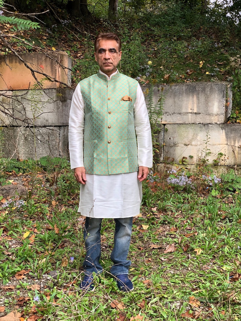 Peut inclure: Un homme portant un gilet vert clair &agrave; motif dor&eacute; et boutons dor&eacute;s sur une chemise blanche et un jean bleu.