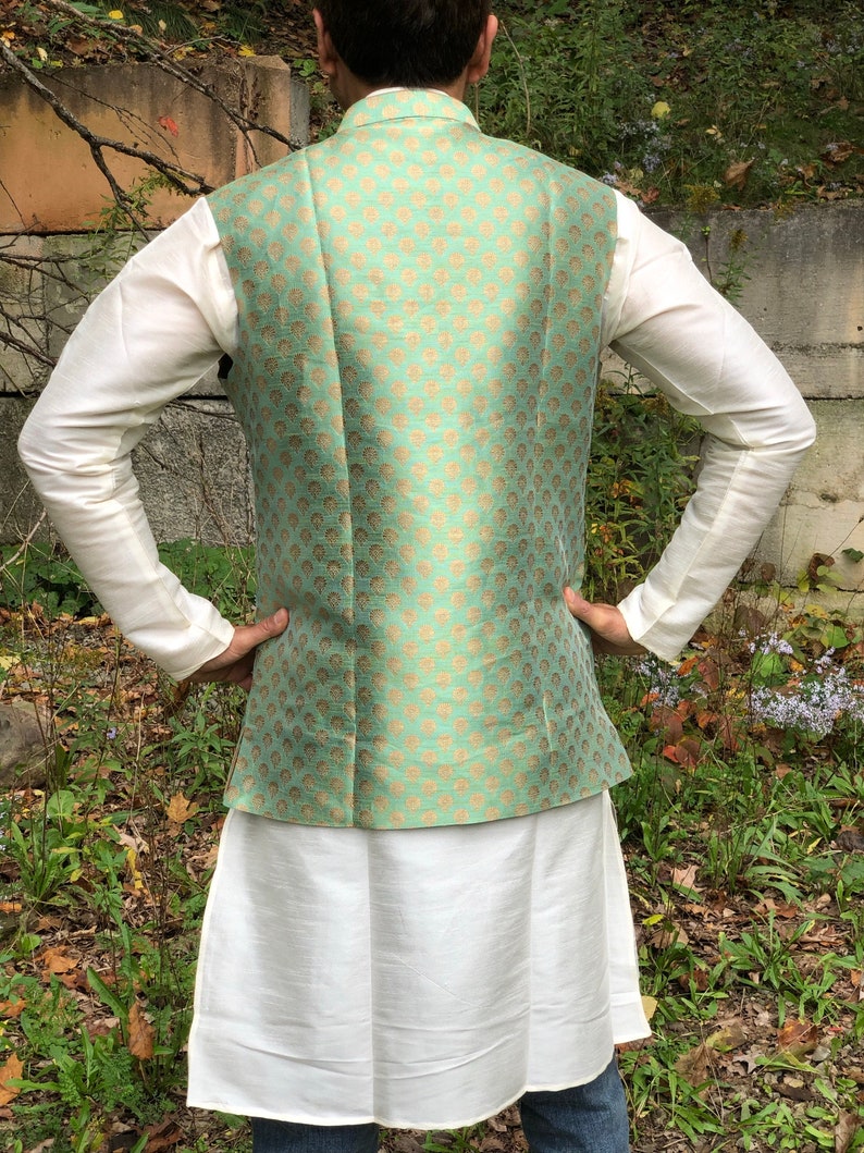 Peut inclure: Un gilet vert menthe avec un motif dor&eacute;. Le gilet est port&eacute; sur une chemise blanche et une longue jupe blanche.