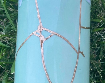 May include: A light blue ceramic vase with gold crackle glaze. The vase has a wide mouth and a cylindrical shape.