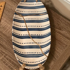 May include: An oval serving tray with blue and white stripes and gold accents. The tray has rope handles and a crack running through the center.