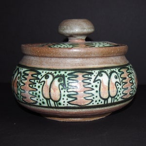 May include: A ceramic jar with a lid, decorated with a repeating pattern of stylized birds in green, pink, and black on a beige background.