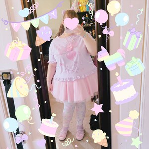 May include: A pink and white tulle skirt with a pink and white graphic tee shirt that says "You're My Favourite" with a pink heart and a pink bow. The person is wearing pink and white patterned tights and pink shoes.