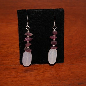 May include: A pair of silver earrings with a white oval shaped stone and a cluster of small purple stones hanging from each.