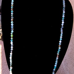 May include: A long necklace made of green, blue, and white gemstone beads. The beads are round and have a smooth, polished finish.