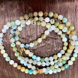 May include: A multi-strand necklace made of green, blue, and white gemstone beads. The beads are strung on a gold chain.