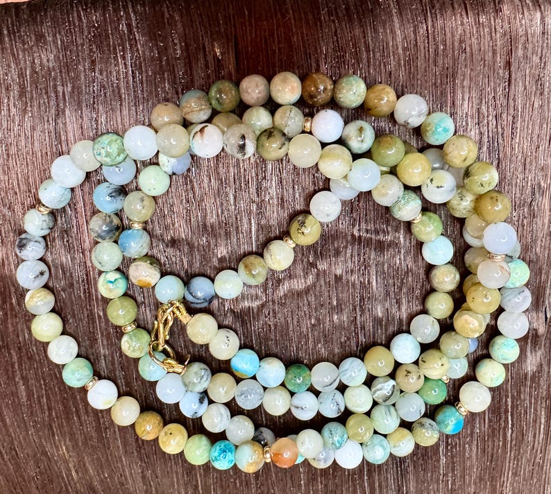 May include: A multi-strand necklace made of green, blue, and white gemstone beads. The beads are strung on a gold chain.