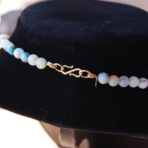 May include: A close-up of a light blue gemstone necklace with a gold clasp. The necklace is displayed on a black velvet stand.