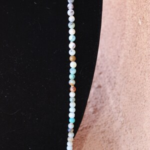 May include: A long strand of turquoise, white, and brown beads on a black background. The beads are round and have a natural, polished look.