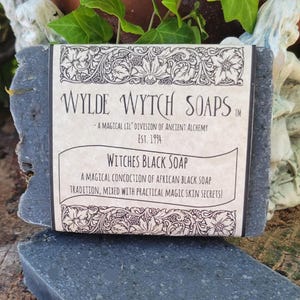 May include: A bar of black soap with a label that reads "WYLDE WYTCH SOAPS - A MAGICAL LIL' DIVISION OF ANCIENT ALCHEMY EST. 1994 WITCHES BLACK SOAP A MAGICAL CONCOCTION OF AFRICAN BLACK SOAP TRADITION, MIXED WITH PRACTICAL MAGIC SKIN SECRETS!"