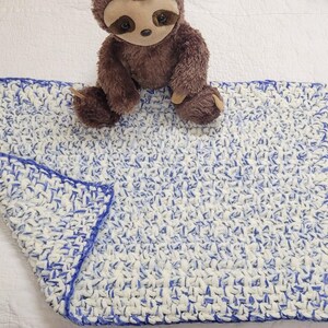 May include: A blue and white crocheted baby blanket with a brown sloth stuffed animal on top.