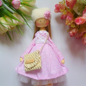 May include: A handmade doll with long brown hair, wearing a pink dress with white polka dots, a white crocheted hat with a pink flower, and a small gold and white purse with the words "Hand Made" on it.