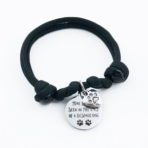 May include: Black paracord bracelet with a silver charm that says "True love is seen in the eyes of a rescued dog" with a paw print heart charm.