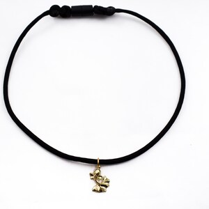 Puede incluir: Un collar gargantilla negro con un colgante dorado en forma de flor estilizada.
