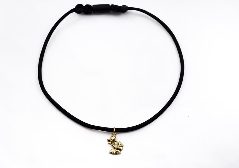 Puede incluir: Un collar gargantilla negro con un colgante dorado en forma de flor estilizada.