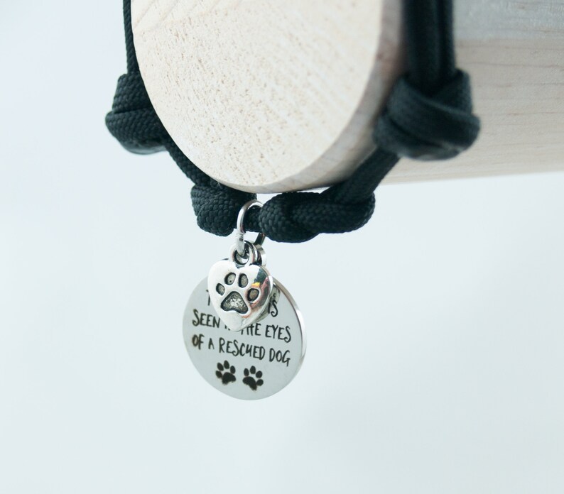 May include: A black paracord bracelet with a silver charm that says "I've seen the eyes of a rescued dog". The charm also has a small paw print heart.