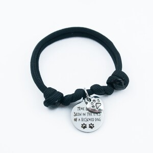 May include: Black paracord bracelet with a silver charm that says "True love is seen in the eyes of a rescued dog" with a paw print heart.