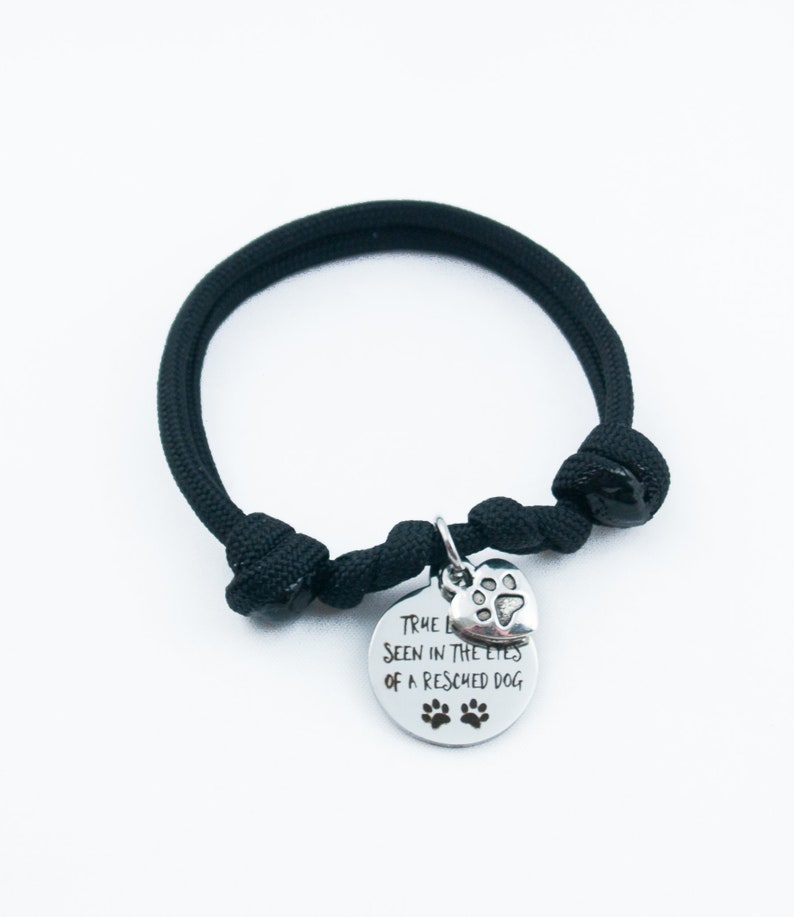May include: Black paracord bracelet with a silver charm that says "True love is seen in the eyes of a rescued dog" with a paw print heart.