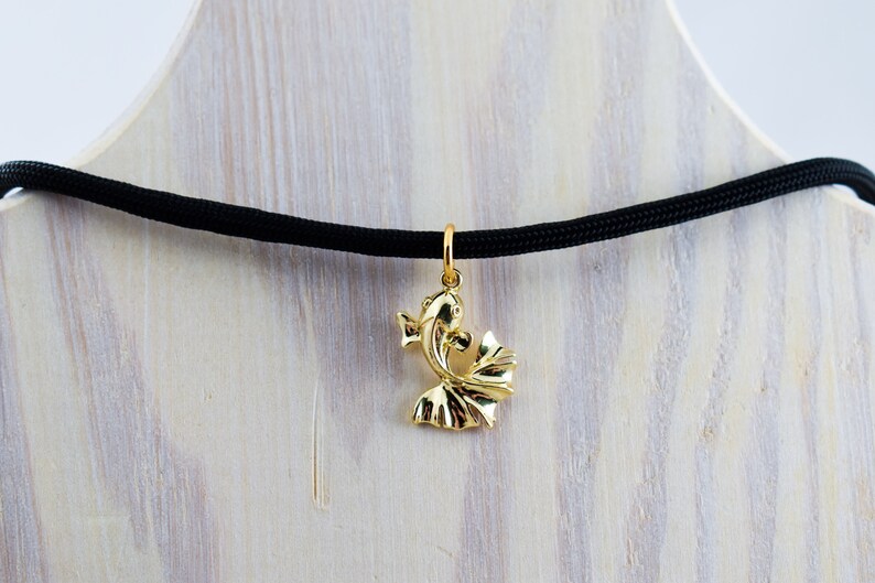 Puede incluir: Un collar con un colgante de pez dorado en un cord&oacute;n negro. El colgante es un dise&ntilde;o tridimensional detallado de un pez con sus aletas caudales extendidas.