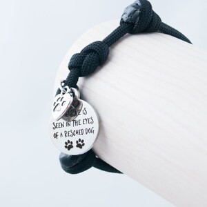 May include: Black paracord bracelet with a silver charm that reads "Love is seen in the eyes of a rescued dog". The charm also has a paw print design.
