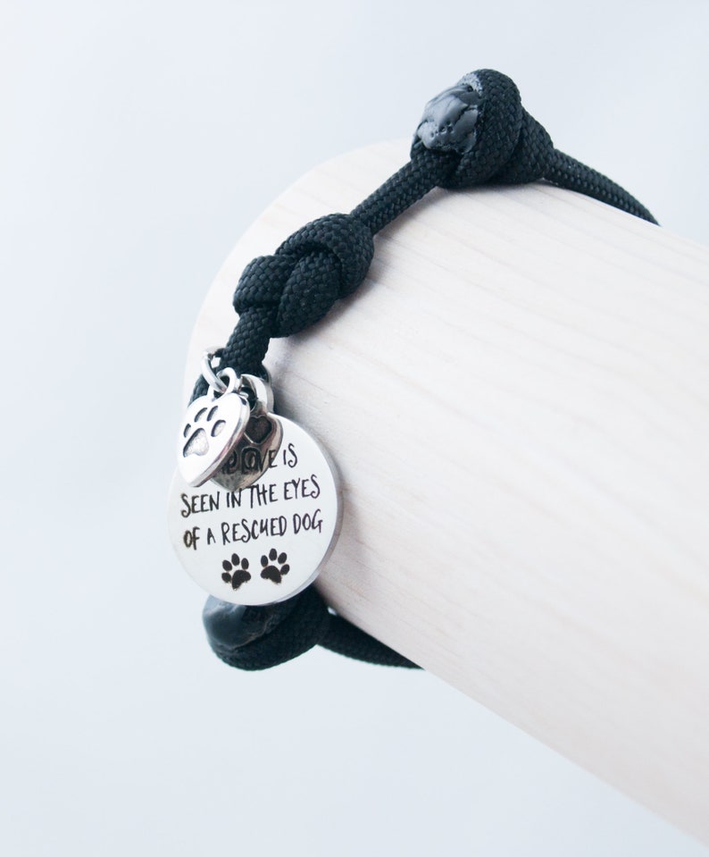 May include: Black paracord bracelet with a silver charm that reads "Love is seen in the eyes of a rescued dog". The charm also has a paw print design.