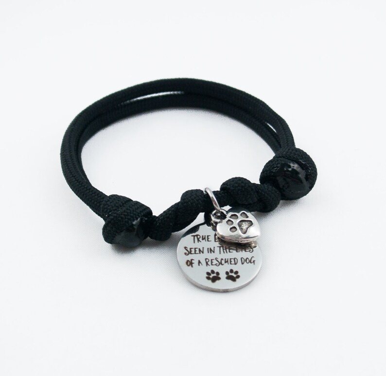 May include: Black paracord bracelet with a silver charm that reads "True love is seen in the eyes of a rescued dog" with a paw print heart.