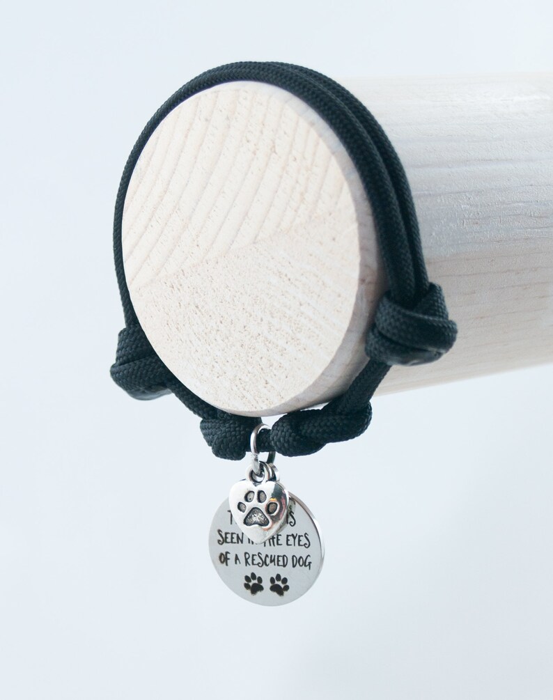 May include: Black paracord bracelet with a silver charm that says "I've seen into the eyes of a rescued dog". The charm has a paw print on it.