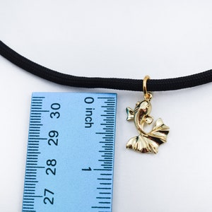 Puede incluir: Un colgante de pez dorado cuelga de un collar de choker el&aacute;stico negro. El colgante mide aproximadamente 2,5 cm de largo y se mide con una regla.