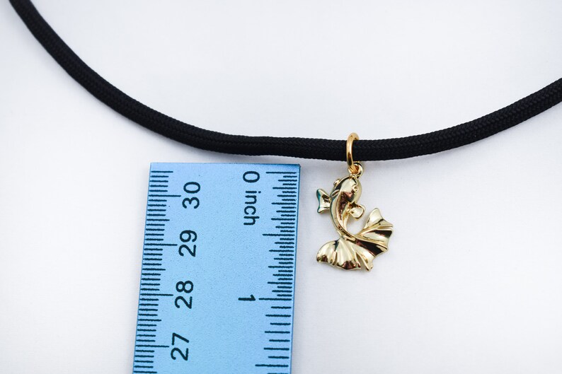 Puede incluir: Un colgante de pez dorado cuelga de un collar de choker el&aacute;stico negro. El colgante mide aproximadamente 2,5 cm de largo y se mide con una regla.