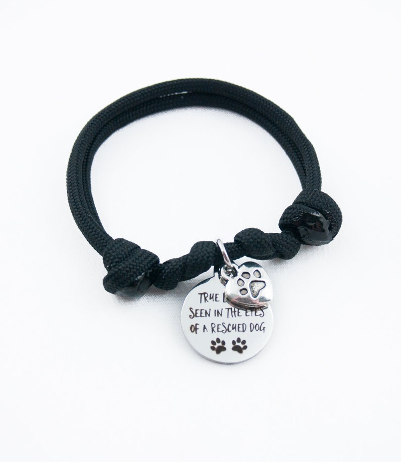 May include: Black paracord bracelet with a silver charm that says "True love is seen in the eyes of a rescued dog" with a paw print heart charm.