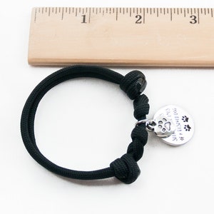 May include: Black paracord bracelet with a silver charm that reads "See the love in the eyes of a rescued dog" with a paw print and three paw prints.