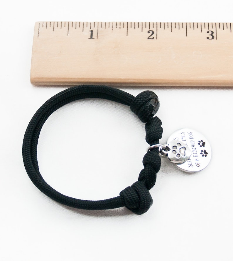 May include: Black paracord bracelet with a silver charm that reads "See the love in the eyes of a rescued dog" with a paw print and three paw prints.