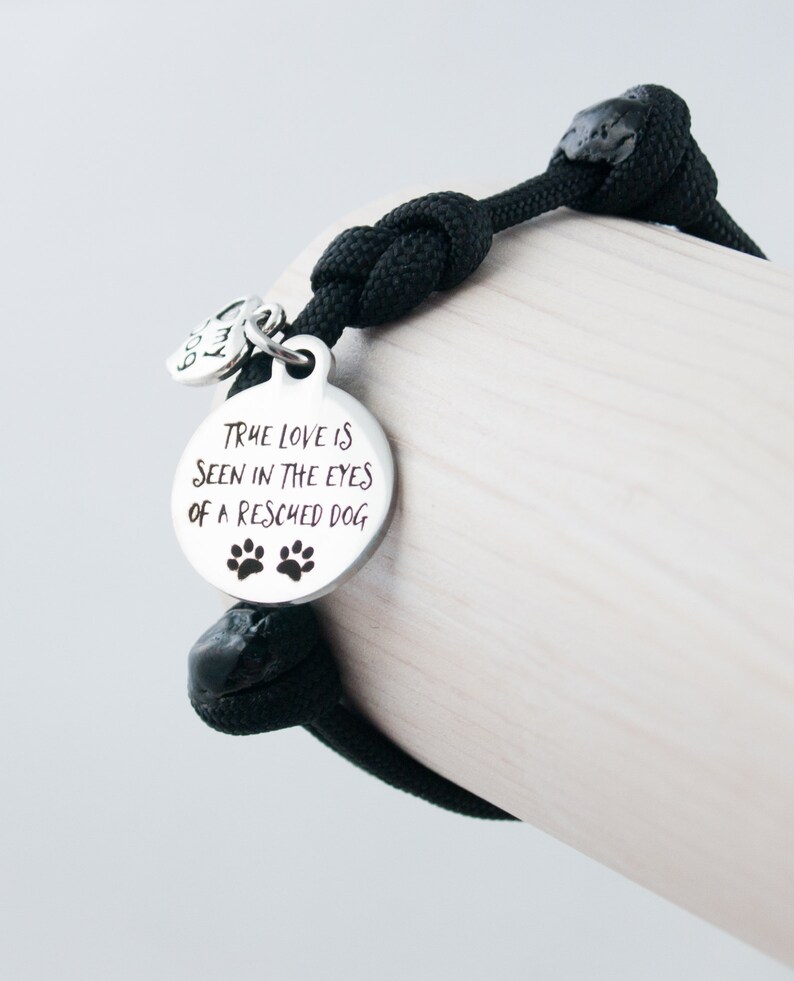 May include: Black paracord bracelet with a silver charm that reads "True love is seen in the eyes of a rescued dog" with two paw prints.