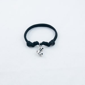 May include: A black paracord bracelet with a silver charm of a pair of binoculars.