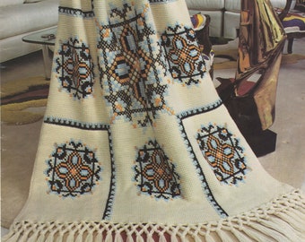 Può includere: Una coperta di uncinetto bianca con un bordo a frangia. La coperta presenta un motivo ripetuto di quadrati ricamati con disegni geometrici in blu, nero, arancione e giallo. Il testo "Embroidered SCANDIA" è visibile nell'angolo in alto a destra dell'immagine.