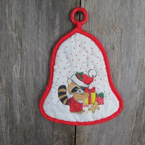 May include: A white fabric Christmas bell ornament with a red trim. The bell features a cartoon raccoon wearing a Santa hat and holding a gift. The bell has a red loop at the top for hanging.