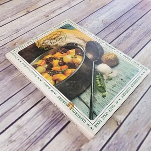 May include: A white cookbook with a green border and the title "Woman's Day Encyclopedia of Cookery, Vol. 2" on the spine. The cover features a photo of a pot of stew with vegetables and meat.